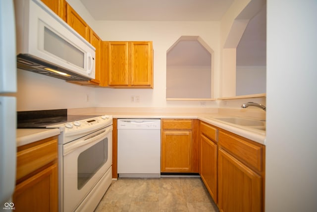 kitchen featuring brown cabinetry, a sink, white appliances, and light countertops