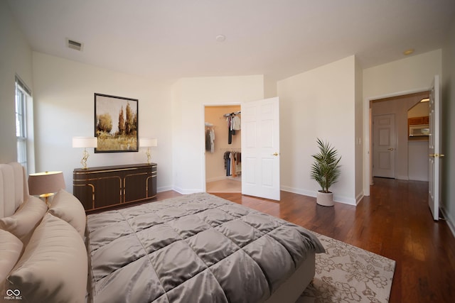 bedroom with a walk in closet, visible vents, wood finished floors, baseboards, and a closet