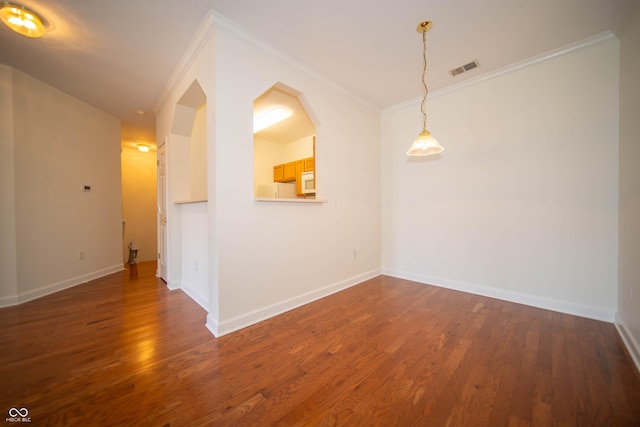 spare room with crown molding, baseboards, wood finished floors, and visible vents
