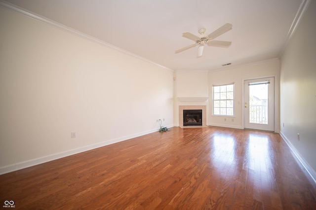 unfurnished living room featuring crown molding, wood finished floors, baseboards, a tiled fireplace, and a ceiling fan