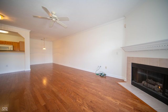 unfurnished living room featuring a tiled fireplace, ornamental molding, ceiling fan, and wood finished floors