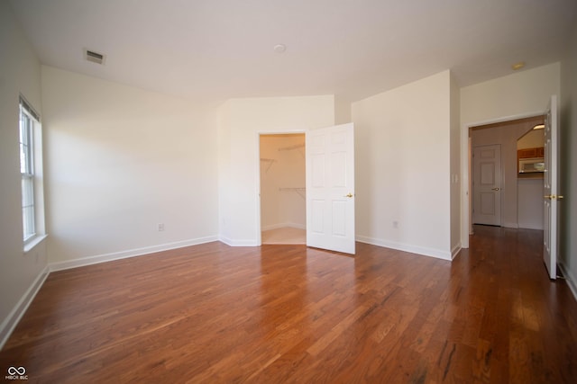 unfurnished bedroom featuring dark wood-style flooring, baseboards, visible vents, and a walk in closet
