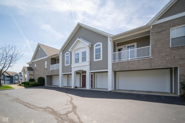view of property featuring a garage, aphalt driveway, a balcony, brick siding, and a residential view