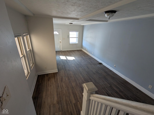 empty room with dark wood-type flooring, a textured ceiling, baseboards, and visible vents