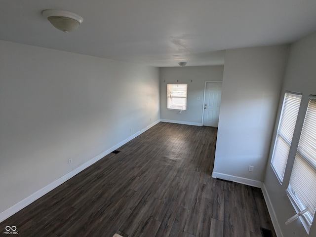 empty room featuring dark wood-type flooring, baseboards, and visible vents