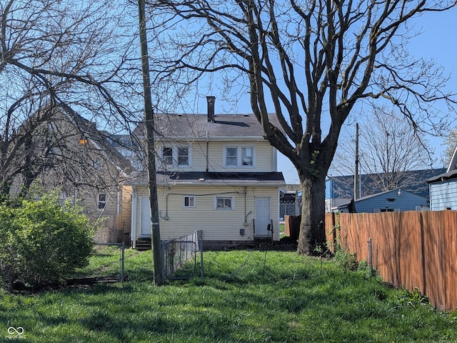 back of house featuring entry steps, fence, a yard, and a chimney