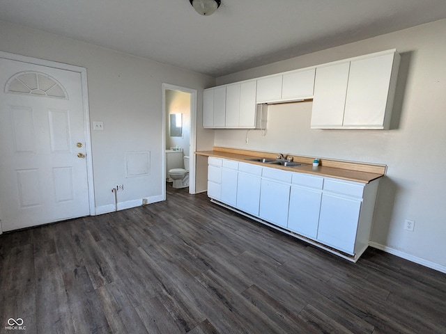 kitchen featuring dark wood-type flooring, white cabinets, a sink, and baseboards