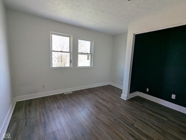 empty room with a textured ceiling, dark wood-style flooring, baseboards, and visible vents