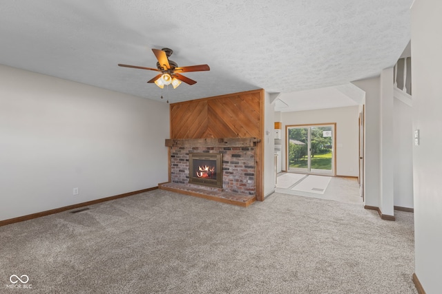 unfurnished living room featuring a ceiling fan, carpet floors, baseboards, a fireplace, and a textured ceiling