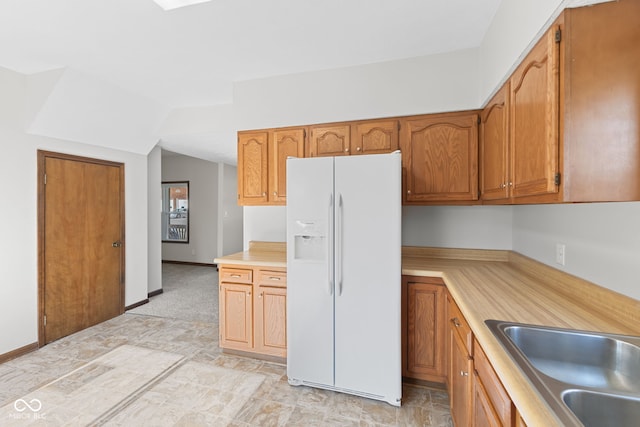 kitchen featuring white fridge with ice dispenser, light countertops, brown cabinets, and a sink