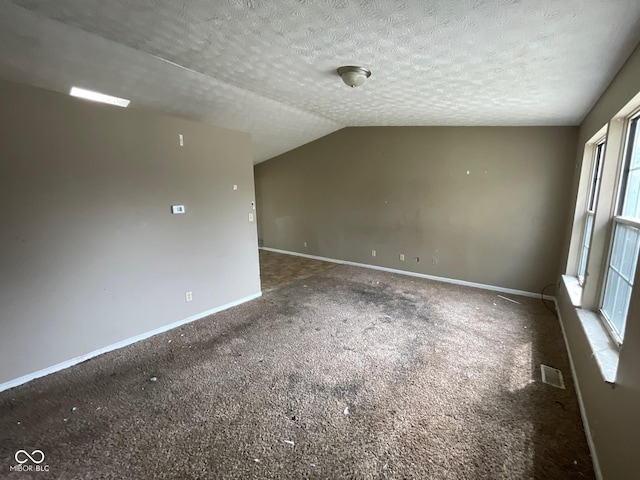empty room featuring a textured ceiling, vaulted ceiling, baseboards, visible vents, and carpet floors