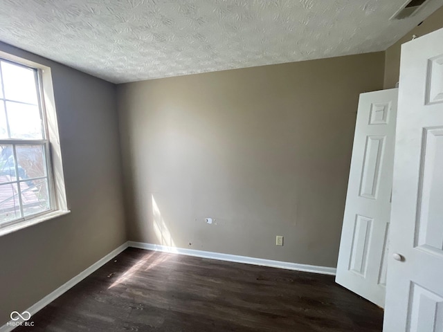 spare room with dark wood finished floors, baseboards, a textured ceiling, and visible vents