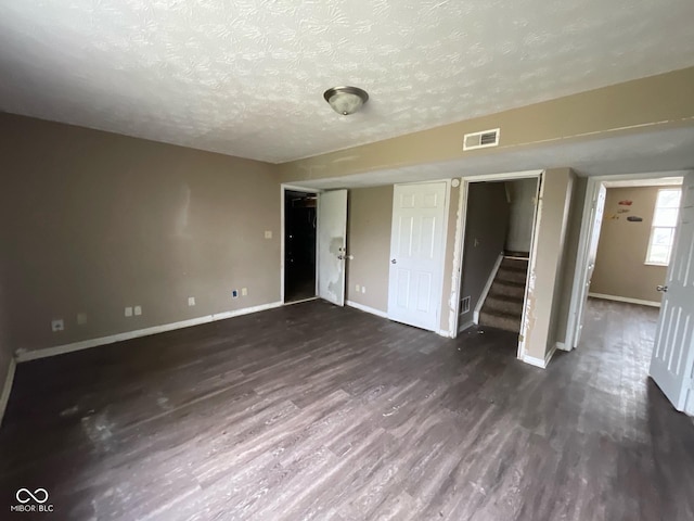 unfurnished bedroom featuring dark wood finished floors, baseboards, a textured ceiling, and visible vents
