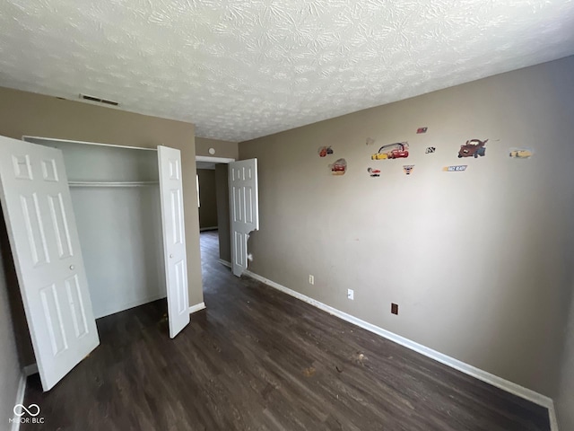 unfurnished bedroom featuring a textured ceiling, a closet, dark wood finished floors, baseboards, and visible vents