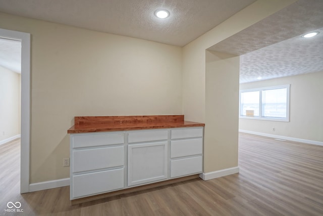 corridor featuring a textured ceiling, baseboards, recessed lighting, and light wood finished floors