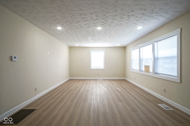 empty room featuring visible vents, a textured ceiling, baseboards, and wood finished floors