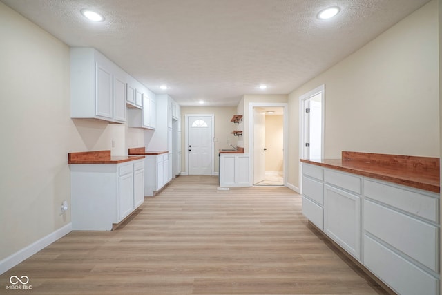 kitchen with butcher block counters, baseboards, a textured ceiling, white cabinets, and light wood finished floors