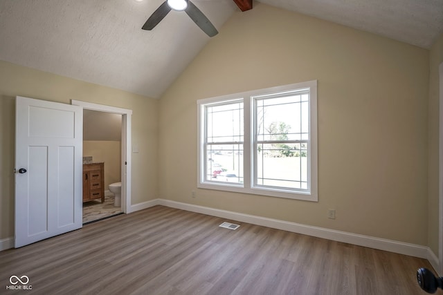 unfurnished bedroom with ensuite bath, baseboards, vaulted ceiling with beams, wood finished floors, and visible vents