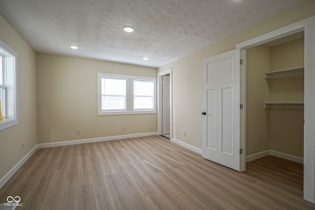 unfurnished bedroom featuring a walk in closet, a textured ceiling, recessed lighting, baseboards, and light wood-type flooring