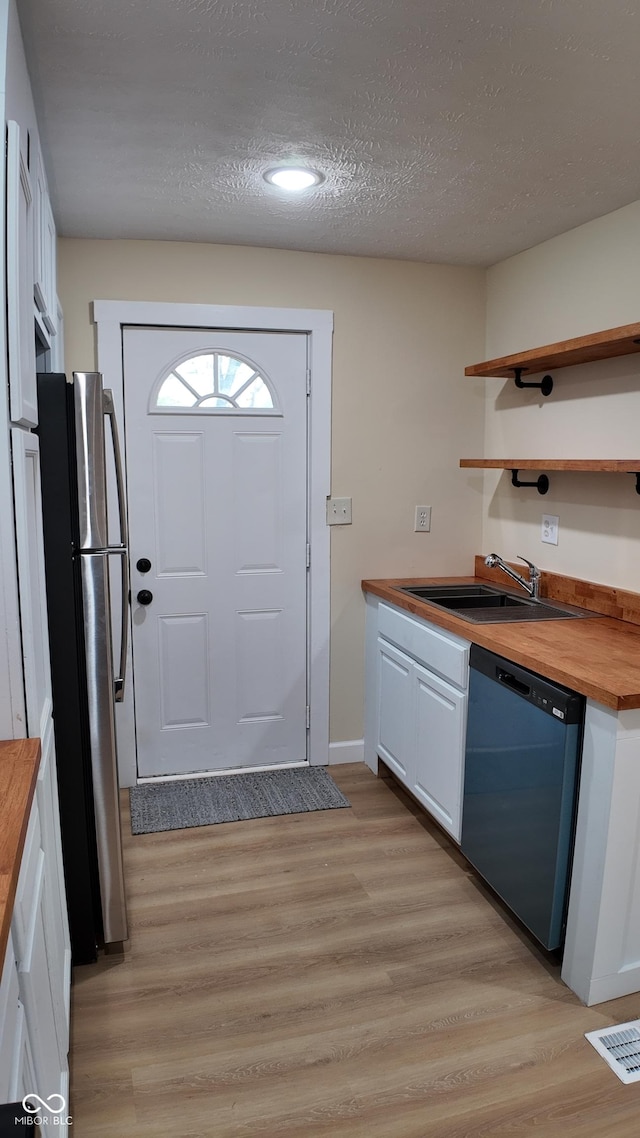 kitchen with dishwasher, a sink, white cabinets, freestanding refrigerator, and wood counters