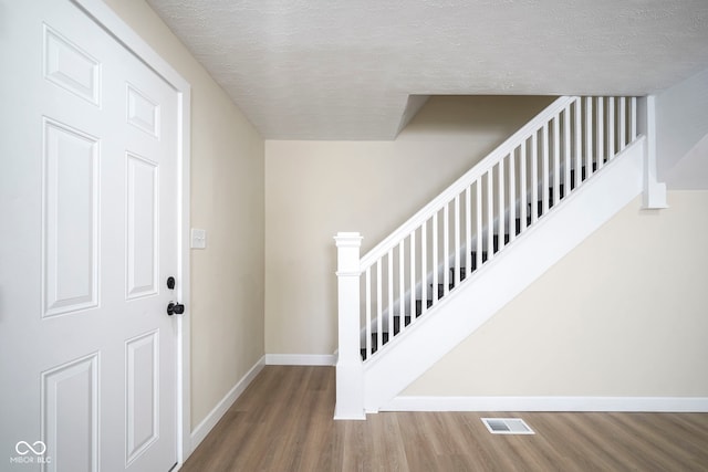 entryway with a textured ceiling, baseboards, visible vents, and wood finished floors
