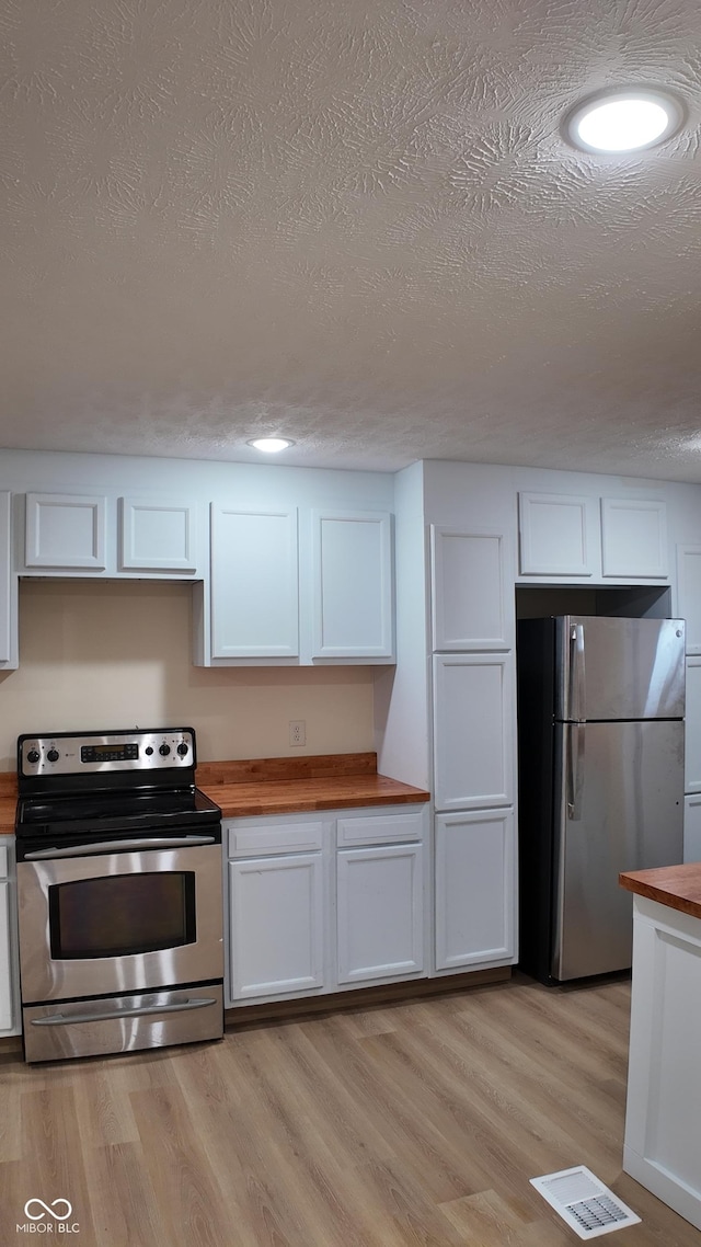 kitchen featuring white cabinets, appliances with stainless steel finishes, light wood finished floors, a textured ceiling, and wood counters