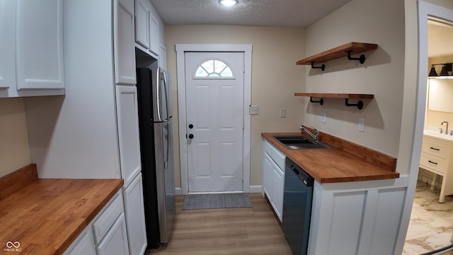 kitchen featuring open shelves, freestanding refrigerator, wooden counters, black dishwasher, and a sink