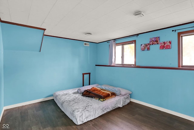 bedroom featuring dark wood-style floors, baseboards, ornamental molding, and visible vents