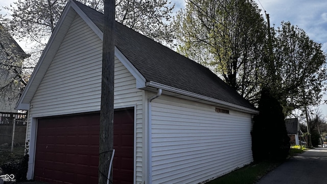 view of side of home featuring roof with shingles, an outdoor structure, and a garage