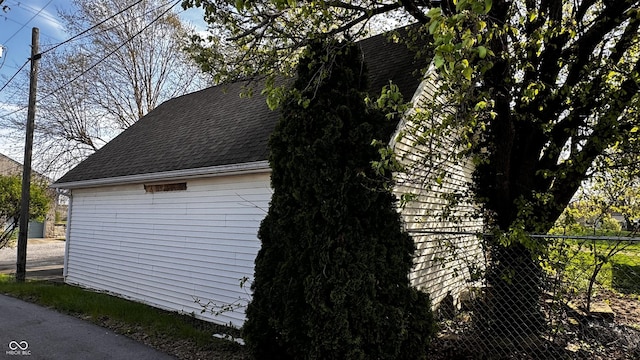 view of side of home with fence and roof with shingles
