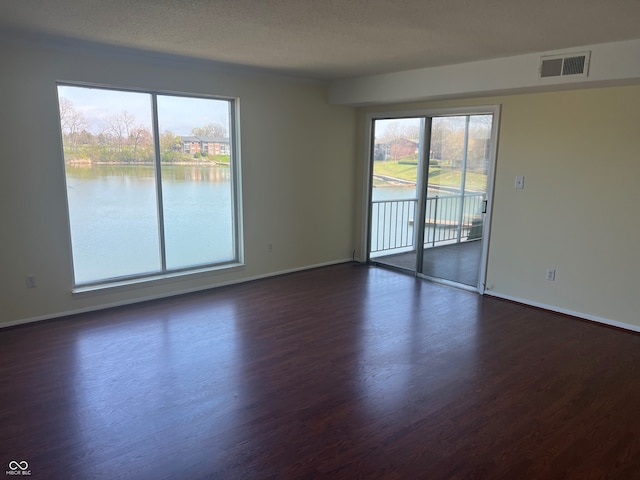 unfurnished room featuring dark wood-style floors, visible vents, a water view, and baseboards