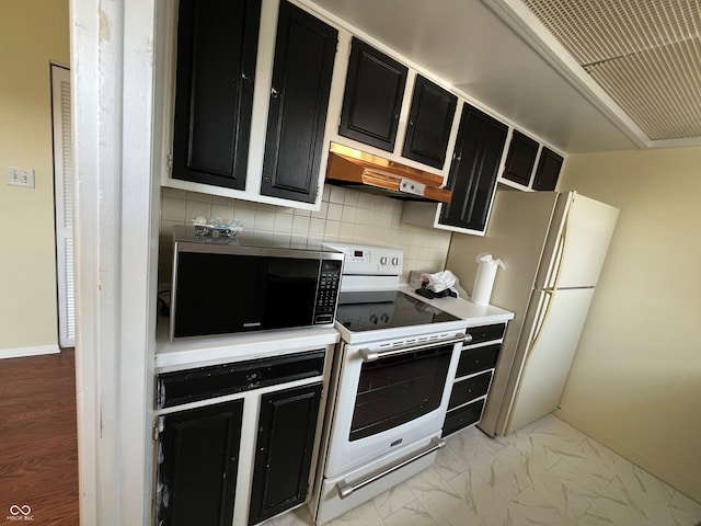 kitchen with dark cabinets, backsplash, under cabinet range hood, and white appliances