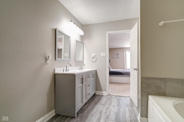 10597 Cyrus Dr, Indianapolis, IN 46231 - ensuite bathroom with wood finished floors, a textured ceiling, double vanity, a bath, and baseboards