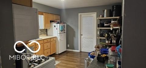 kitchen with light countertops, backsplash, freestanding refrigerator, light brown cabinetry, and wood finished floors