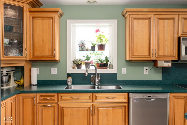kitchen with appliances with stainless steel finishes, a sink, glass insert cabinets, and dark countertops