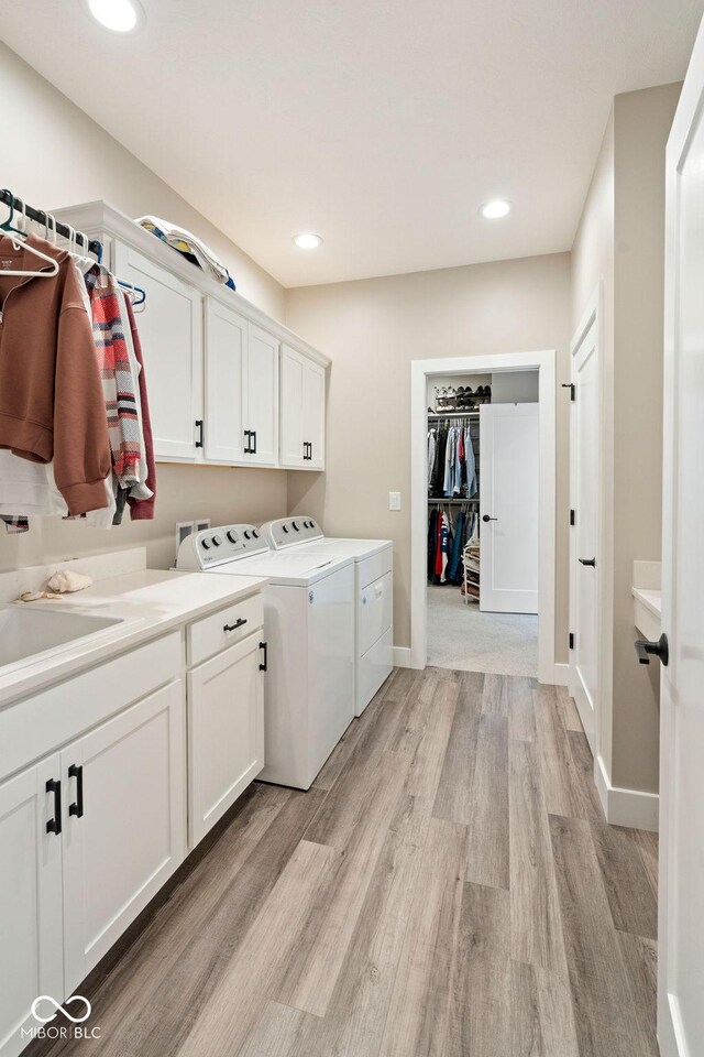 clothes washing area with baseboards, light wood-type flooring, independent washer and dryer, recessed lighting, and cabinet space
