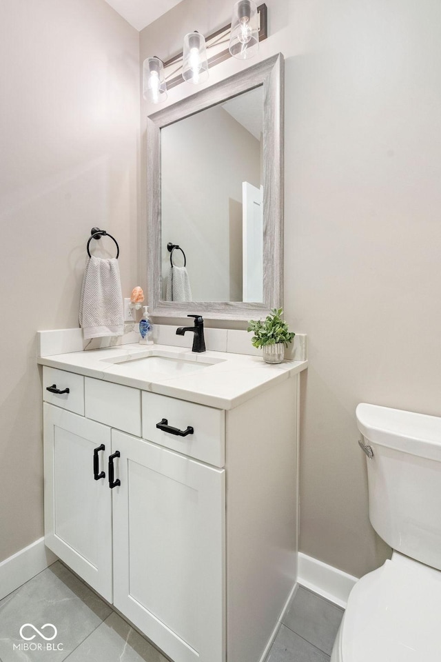 half bath featuring toilet, tile patterned floors, vanity, and baseboards