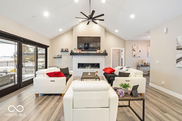 living area with baseboards, ceiling fan, a fireplace, light wood finished floors, and lofted ceiling