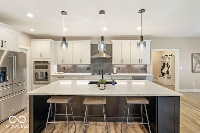 kitchen featuring a kitchen bar, light wood-type flooring, wall chimney range hood, and stainless steel appliances
