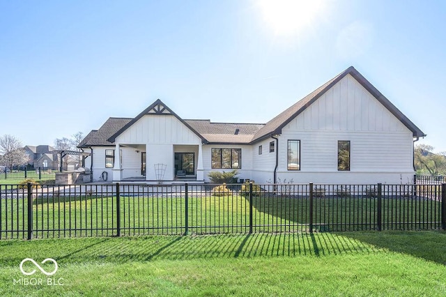 rear view of house with board and batten siding, a fenced front yard, and a lawn