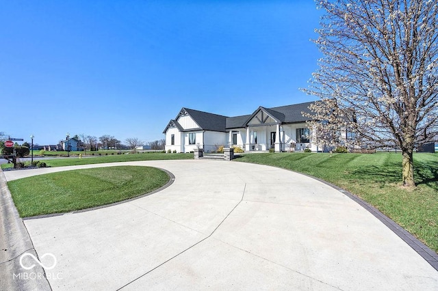 view of front of property featuring board and batten siding, curved driveway, and a front lawn