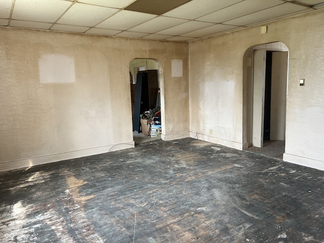 spare room featuring baseboards, arched walkways, and a drop ceiling