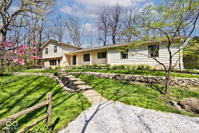 tri-level home featuring stone siding, a front lawn, and fence