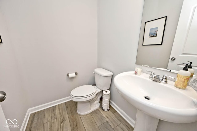 half bathroom with wood finished floors, baseboards, a sink, and toilet