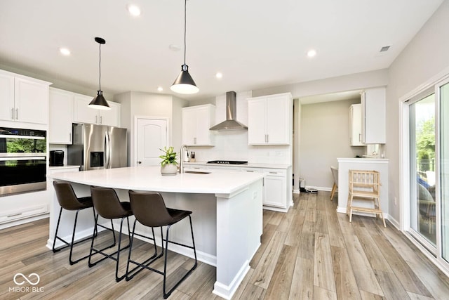 kitchen featuring stainless steel appliances, a sink, backsplash, white cabinetry, and wall chimney range hood