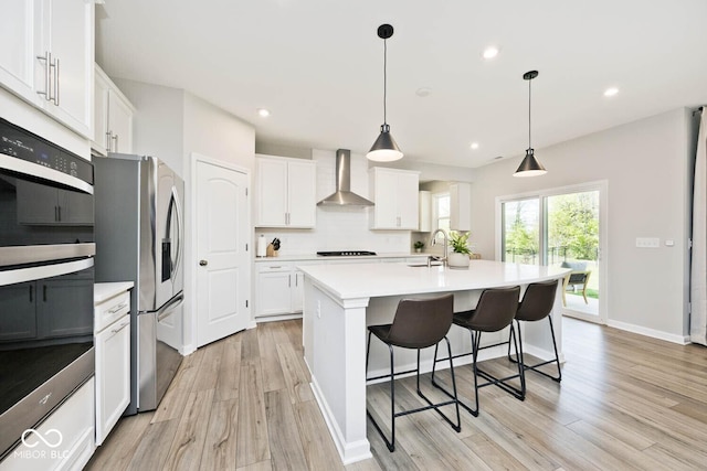kitchen with white cabinets, wall chimney exhaust hood, appliances with stainless steel finishes, and light wood-style floors