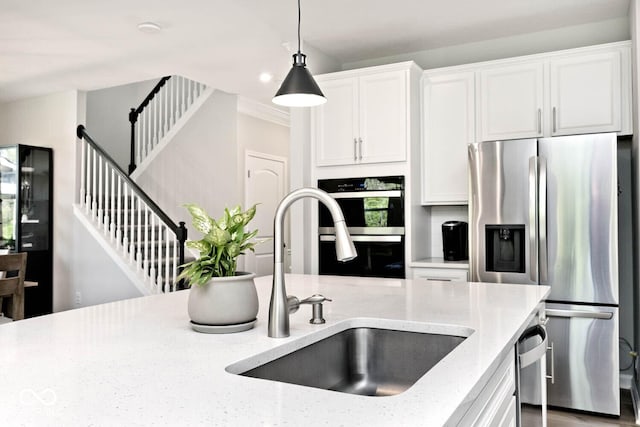 kitchen featuring a sink, white cabinetry, light stone countertops, appliances with stainless steel finishes, and hanging light fixtures