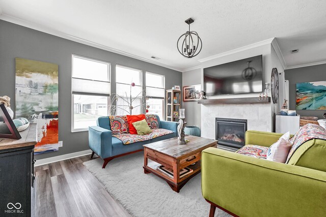 living room featuring wood finished floors, crown molding, a fireplace, baseboards, and a chandelier