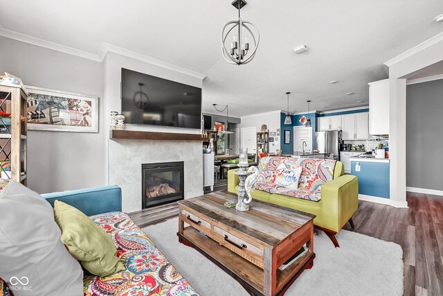 living area with ornamental molding, dark wood-style flooring, a tile fireplace, a chandelier, and baseboards