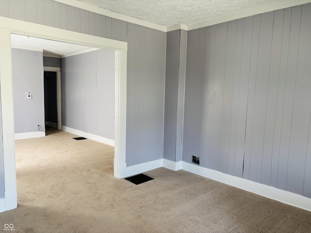 empty room with crown molding, a textured ceiling, visible vents, carpet floors, and wooden walls